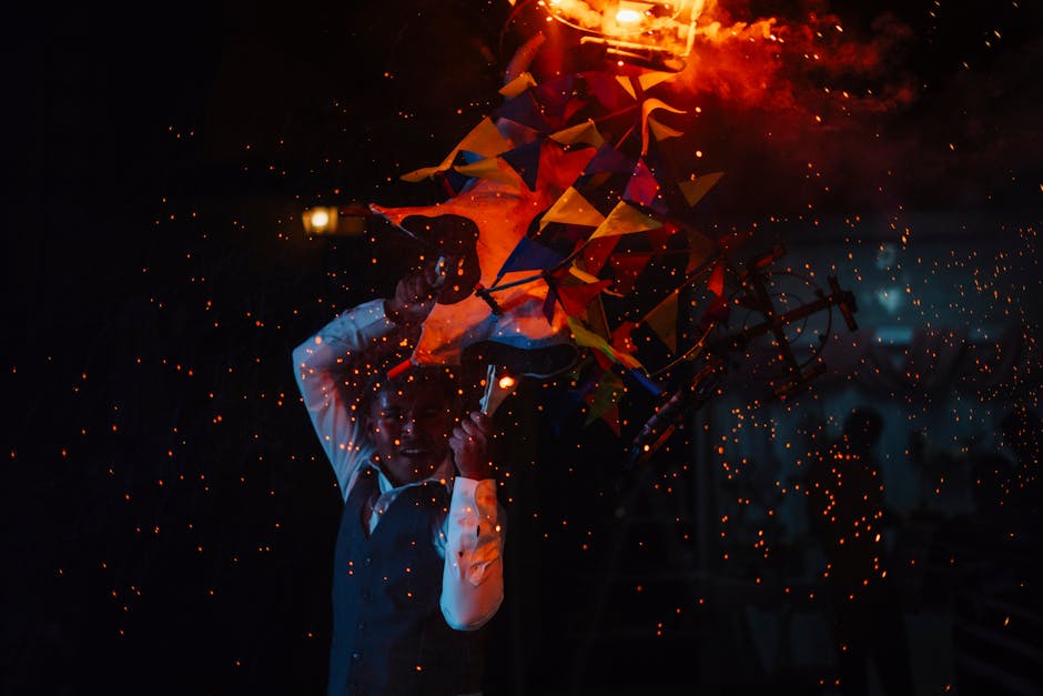 Vibrant fire show at night featuring a performer amidst colorful flags and sparks.
