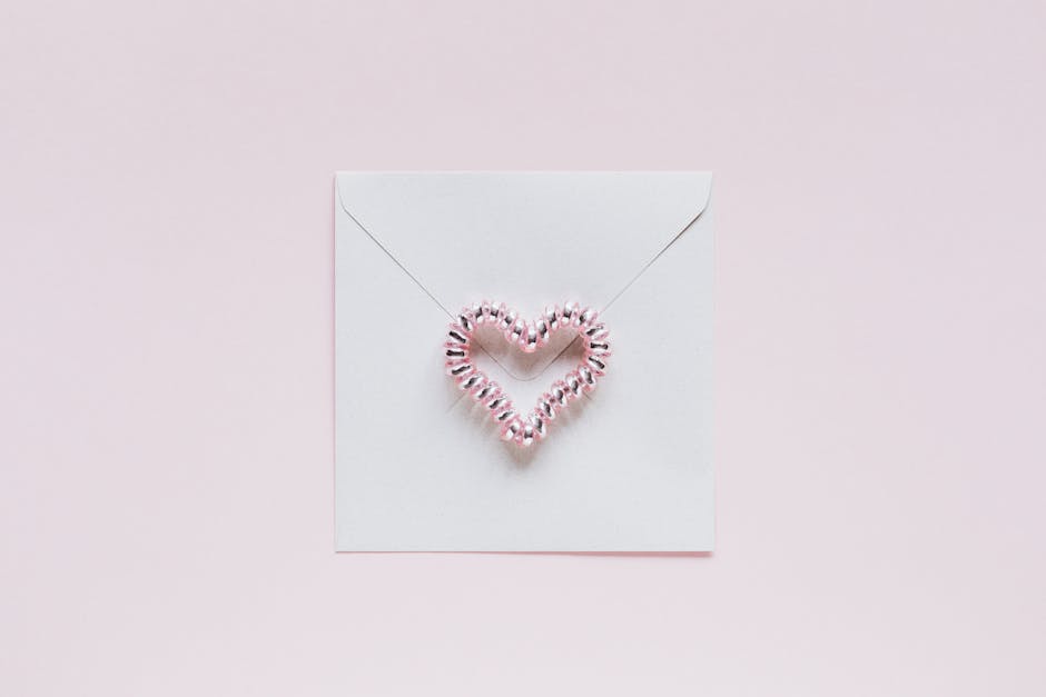 A minimalist design featuring a pink heart decoration on a white envelope with a soft pink background.