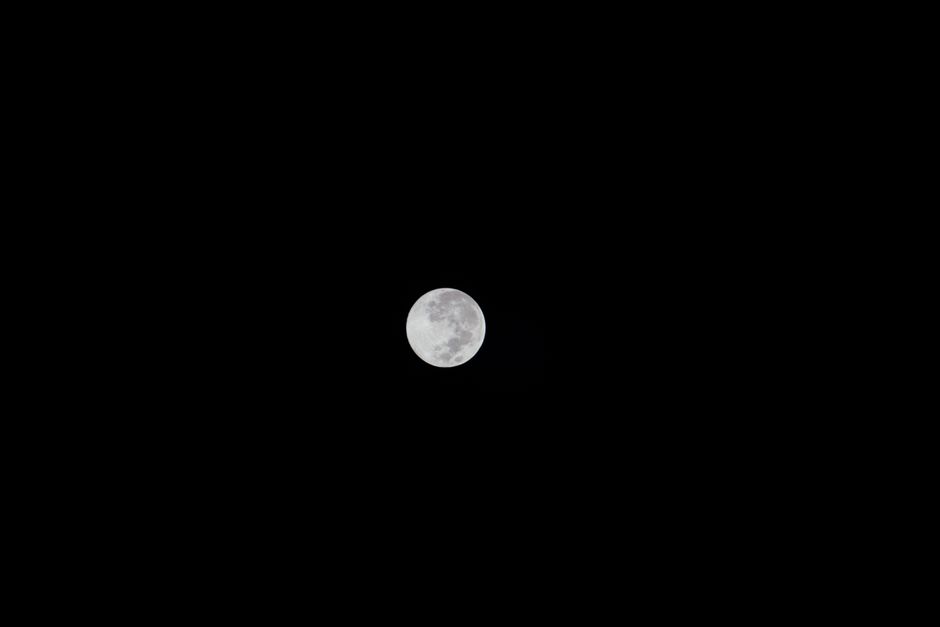 A crisp image of the full moon shining brightly against a dark, clear night sky.