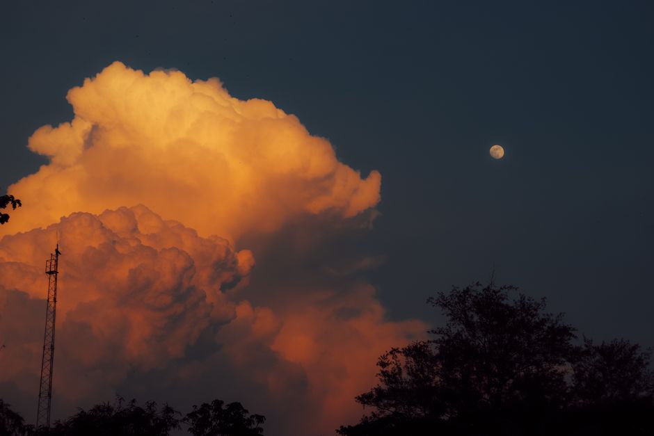 Golden clouds illuminated by sunset with a full moon in the sky, creating a dramatic and serene scene.