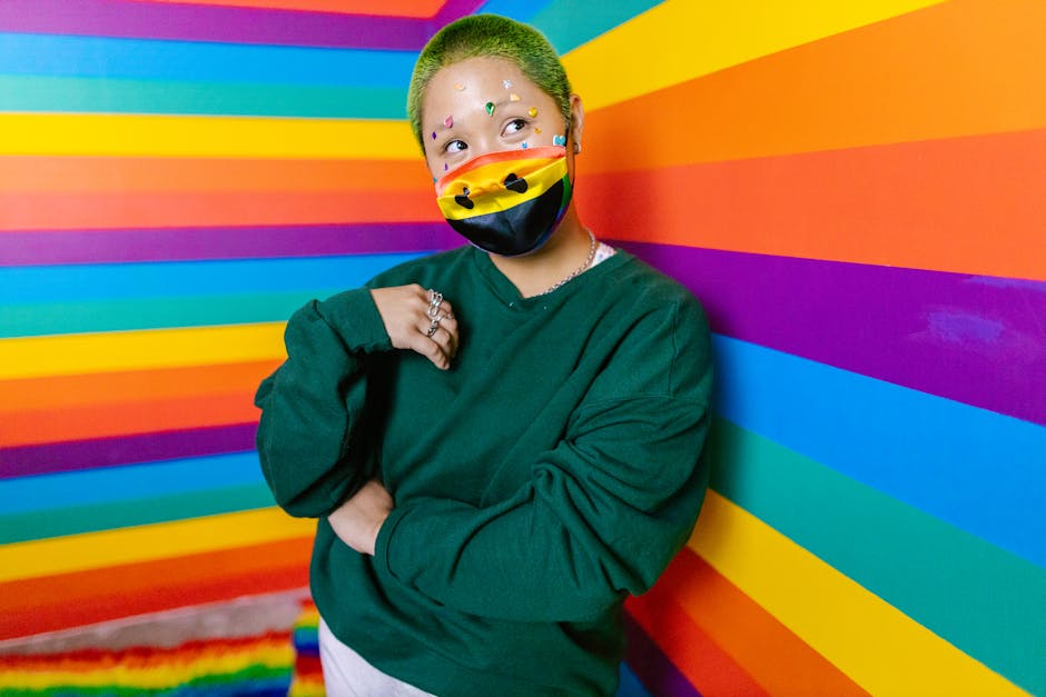 Person with rainbow face mask and dyed hair posing confidently in colorful setting.