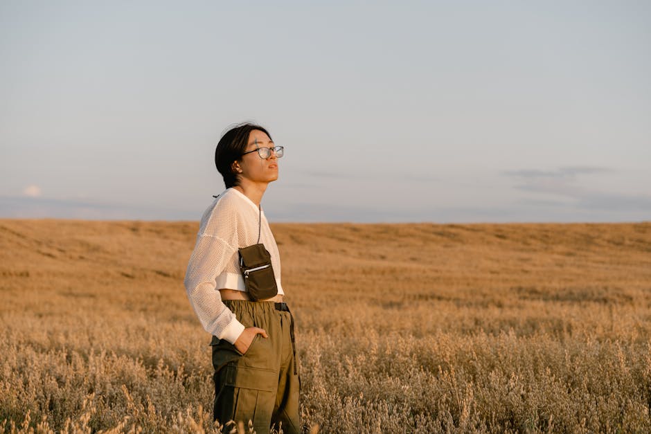 A young woman stands in a golden field at sunset, reflecting serene contemplation.