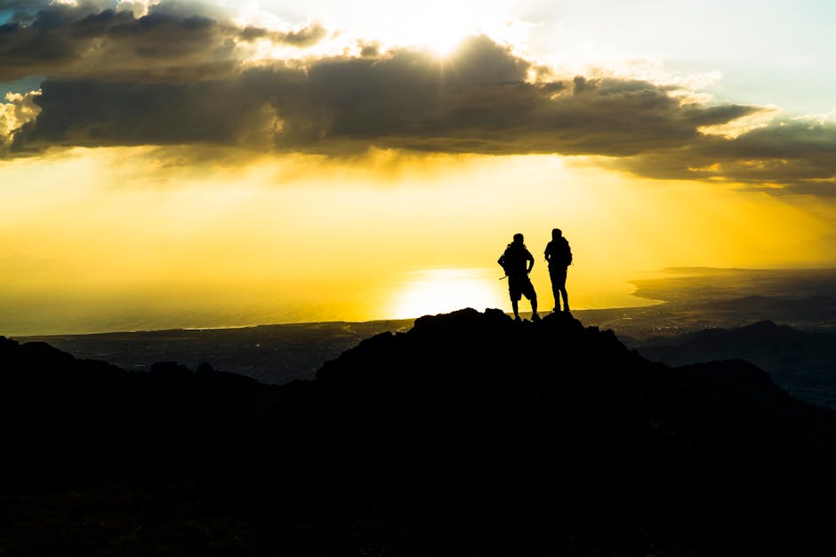 Silhouetted hikers standing on a mountain peak during a stunning sunset.
