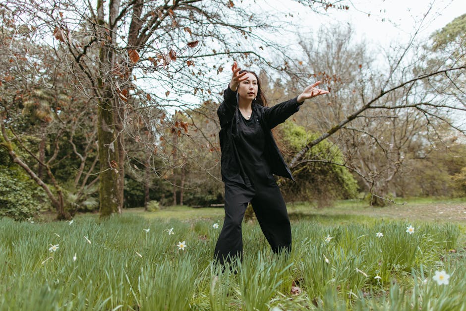 Asian woman gracefully dancing in a tranquil outdoor grass field with scattered trees.