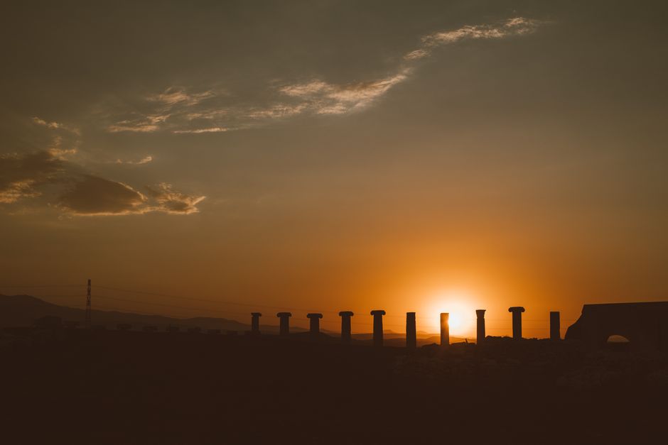 Silhouette of ancient columns against a vivid sunset sky with stunning warm tones.
