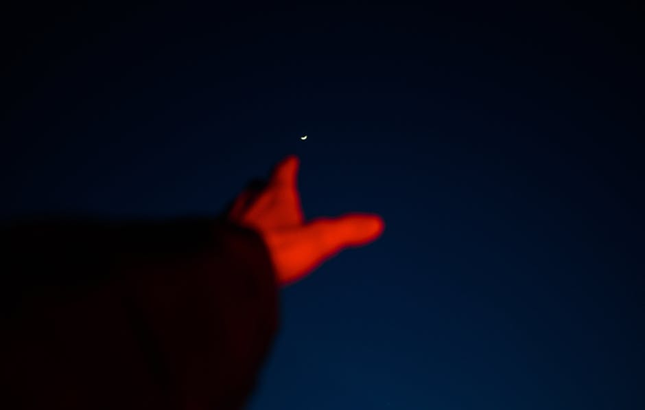 Blurred hand reaching towards a crescent moon in a dark night sky, capturing a sense of aspiration.