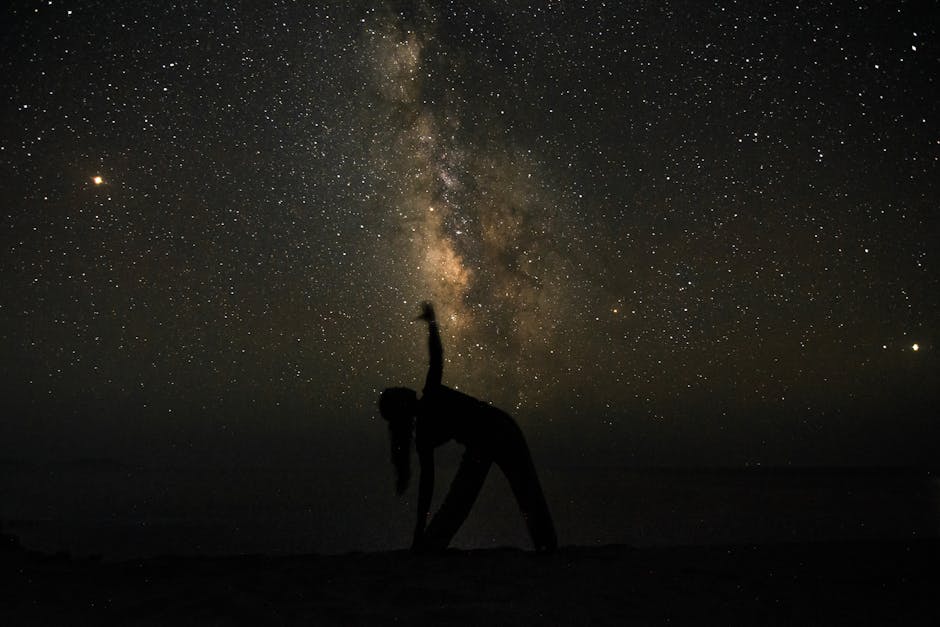 Silhouette of a person practicing yoga beneath the Milky Way