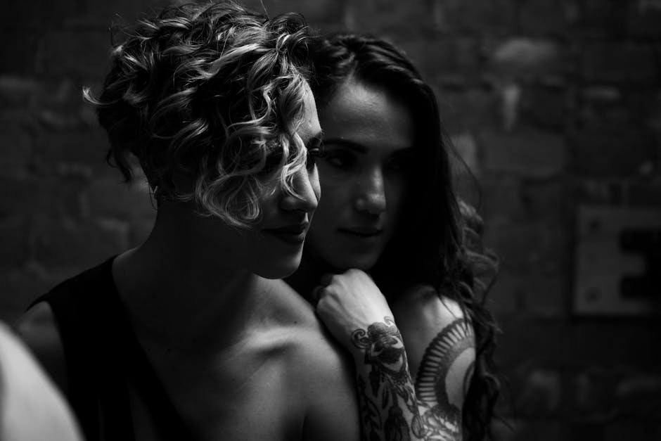Intimate monochrome portrait of two women embracing in low light.
