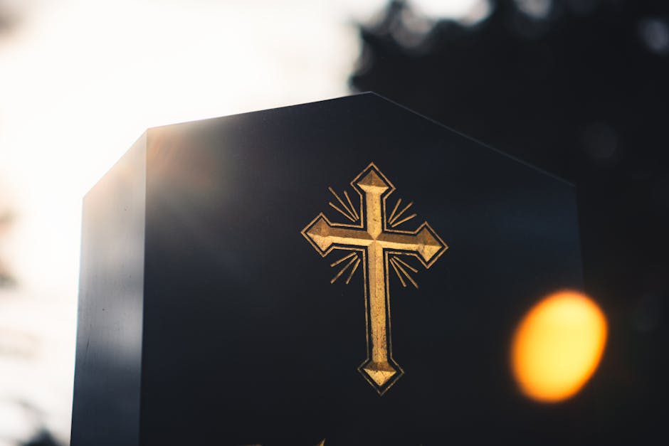 Sunlit golden cross on a stone monument with lens flare, creating a serene and spiritual atmosphere.