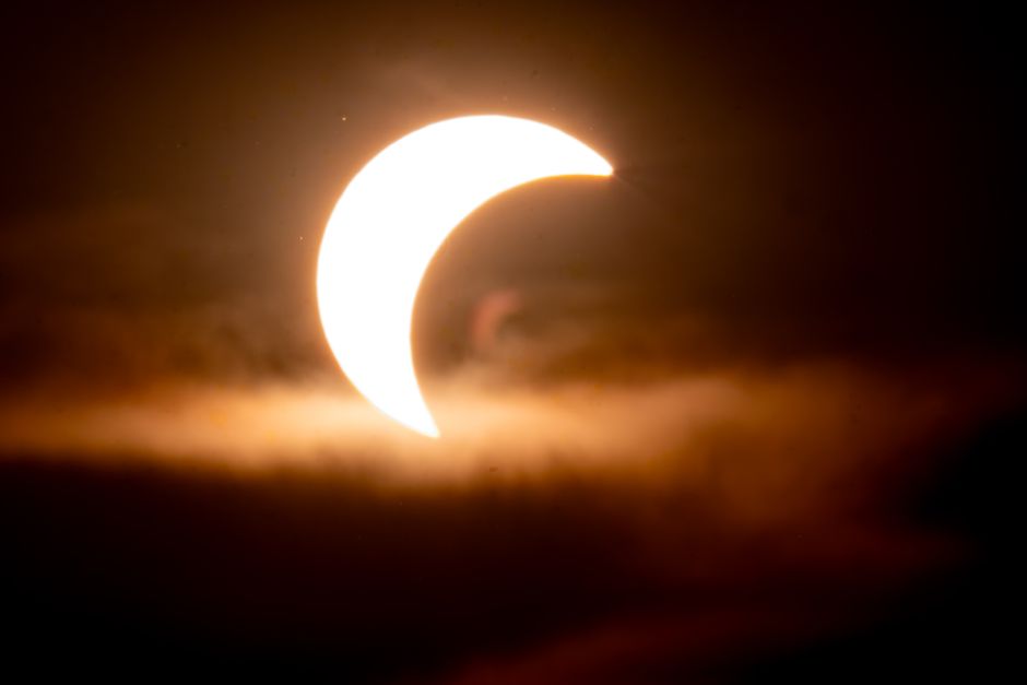 A stunning solar eclipse with a crescent shape glows through clouds, illuminating the night sky.