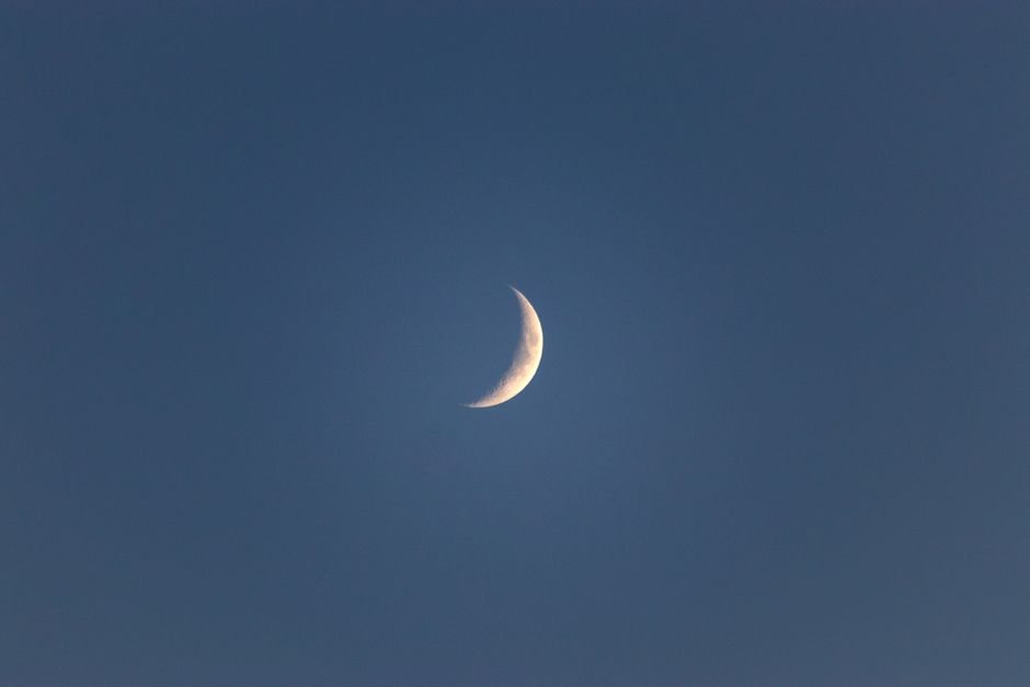 Bright narrow white crescent in blue peaceful sky in late dusky calm evening