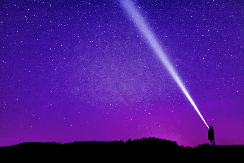 Silhouette of a person shining a flashlight under a starry violet night sky, creating a dramatic scene.