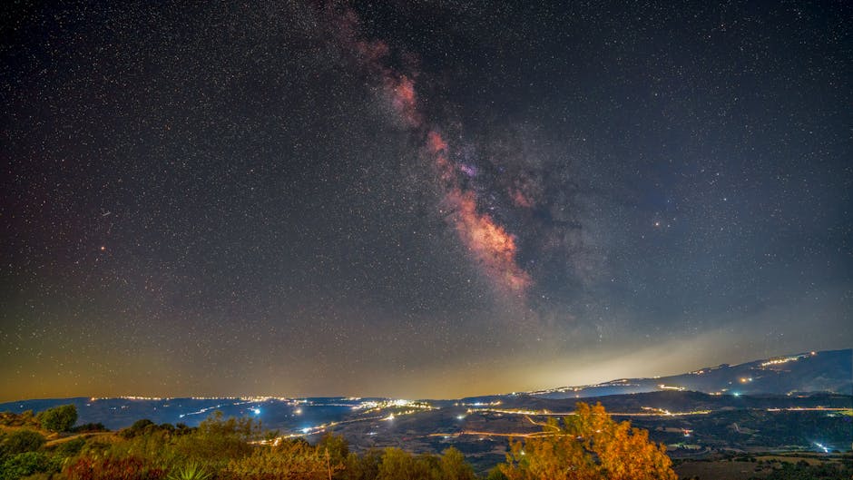 Stunning view of the Milky Way galaxy over a brightly lit landscape at night, showcasing the vastness of space.