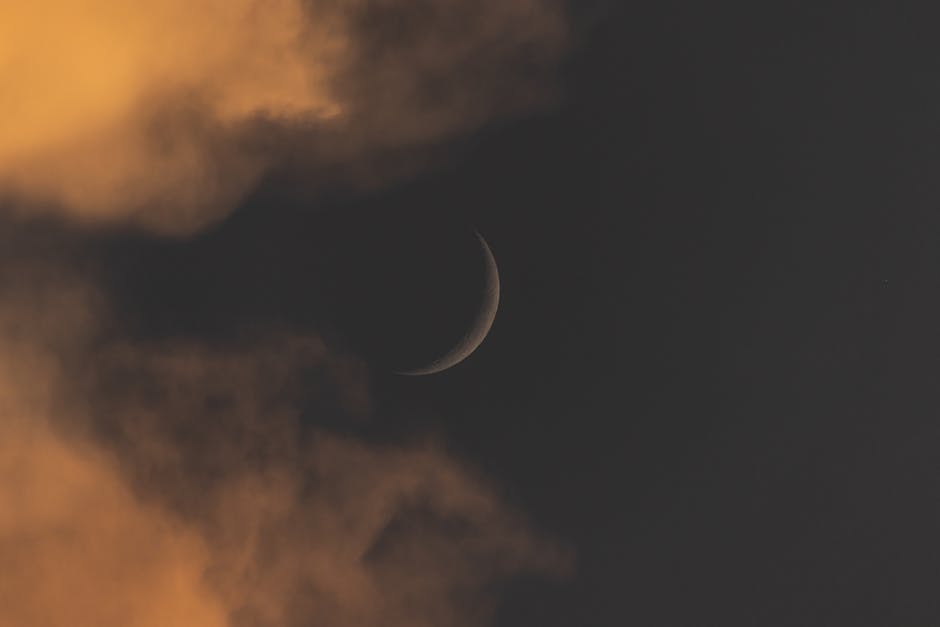 A crescent moon amidst dramatic clouds at night, creating an ethereal mood.