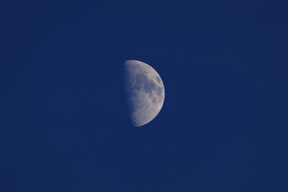 A stunning half moon shining brightly against a clear blue night sky, showcasing crater details.
