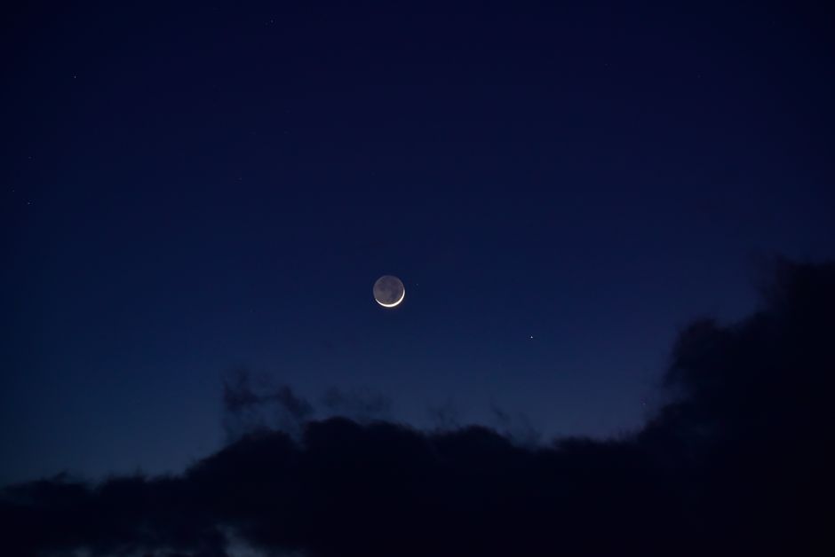A serene crescent moon surrounded by deep blue night sky and fluffy clouds.