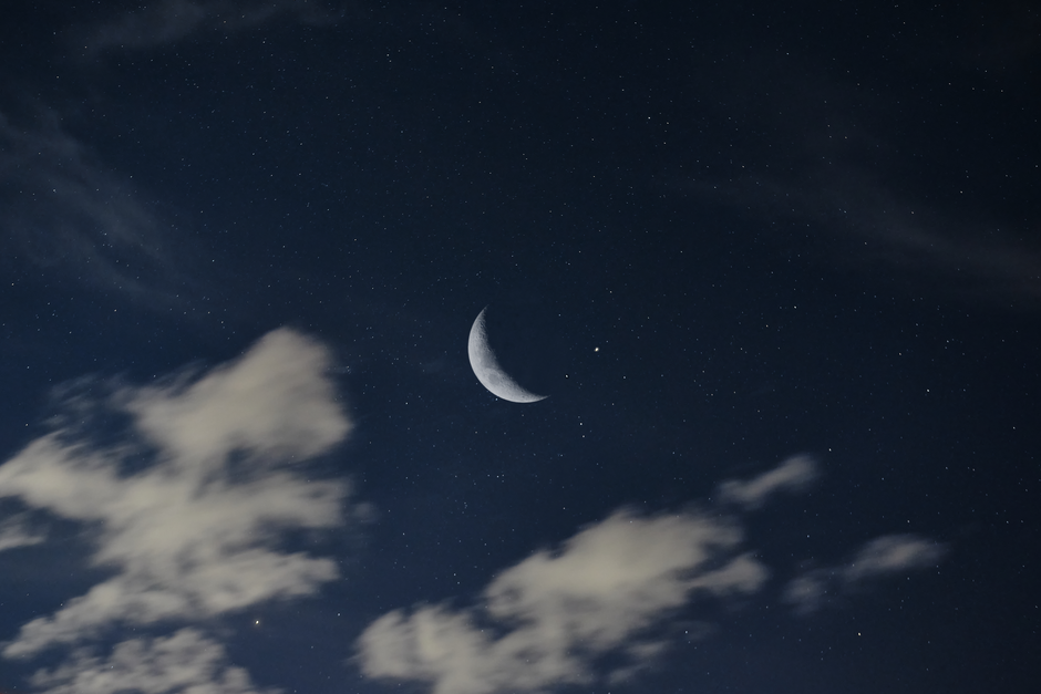 A tranquil night sky with a waning crescent moon among starry clouds.