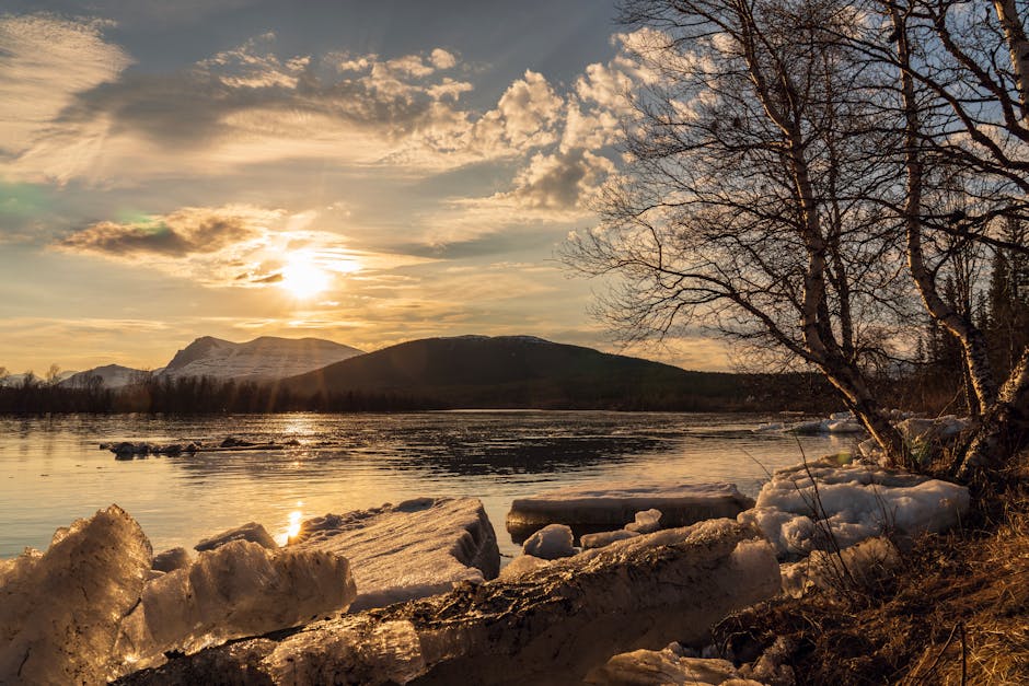 Beautiful winter sunset with ice formations on a serene lake surrounded by mountains.