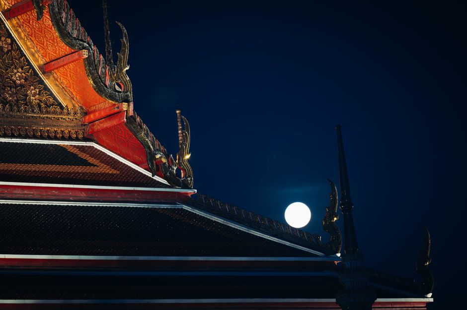 Beautiful traditional Thai temple roof illuminated by full moon. Captures cultural essence of Bangkok.
