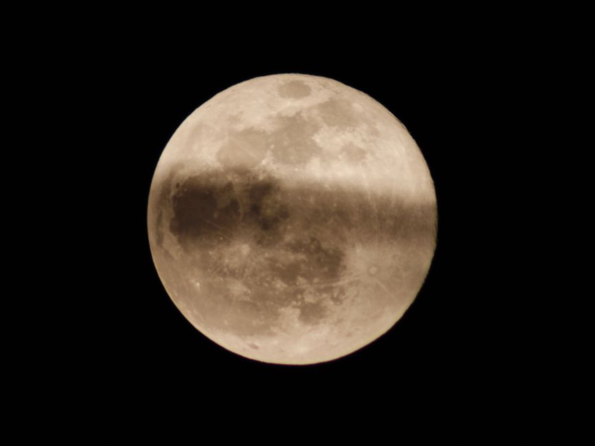 A detailed image of a full moon with a shadow crossing its surface in the night sky.