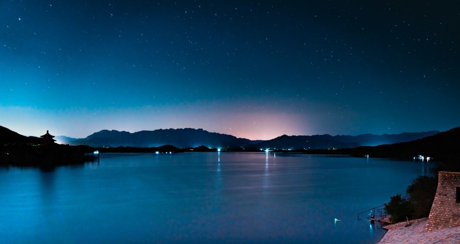 A serene night landscape featuring a starry sky over a calm lake with distant mountains.