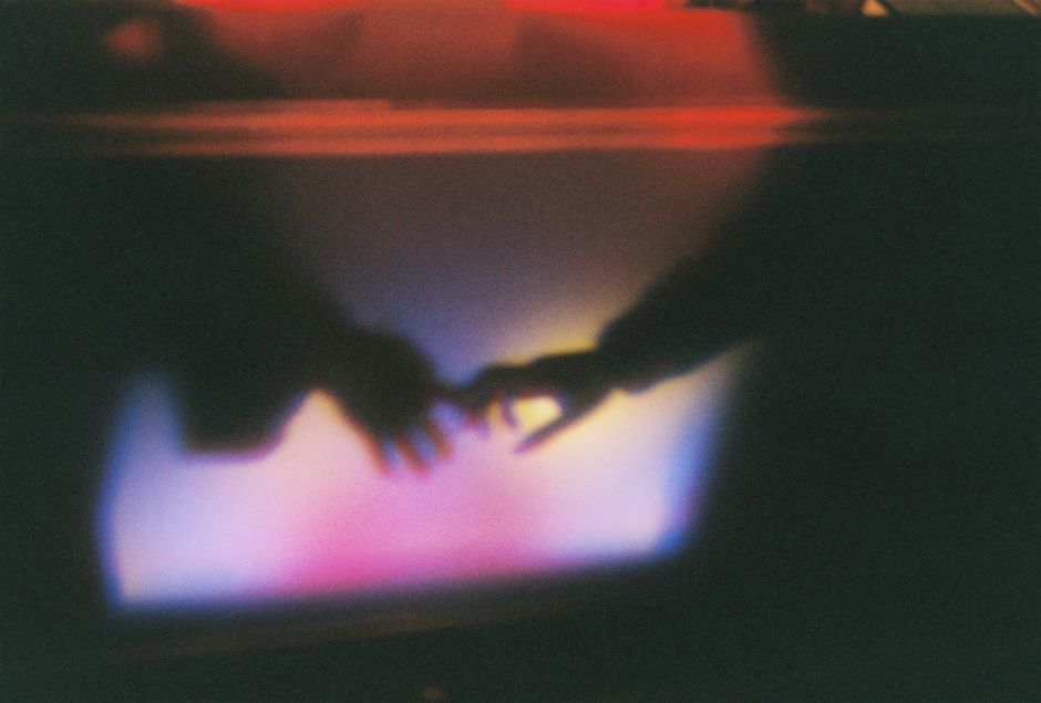 Artistic blurred silhouette of hands reaching towards each other with colorful light effects.
