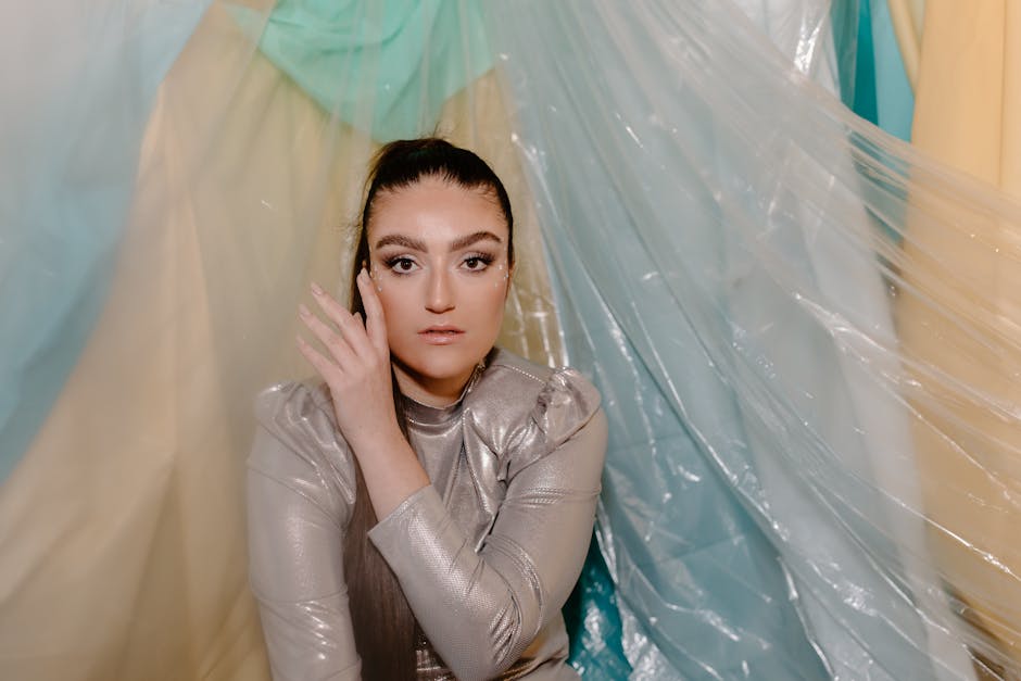 A woman in a silver futuristic outfit posing with pastel drapes background.