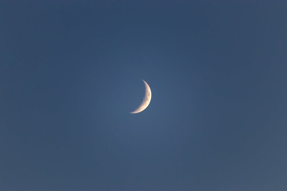 Bright narrow white crescent in blue peaceful sky in late dusky calm evening