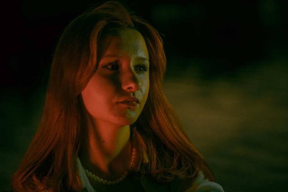 A dramatic portrait of a young redheaded woman with a serious expression under night lighting.
