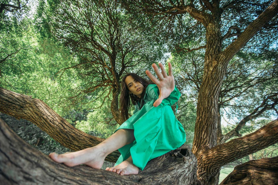 A woman in a green dress sitting on tree branches, surrounded by lush greenery.