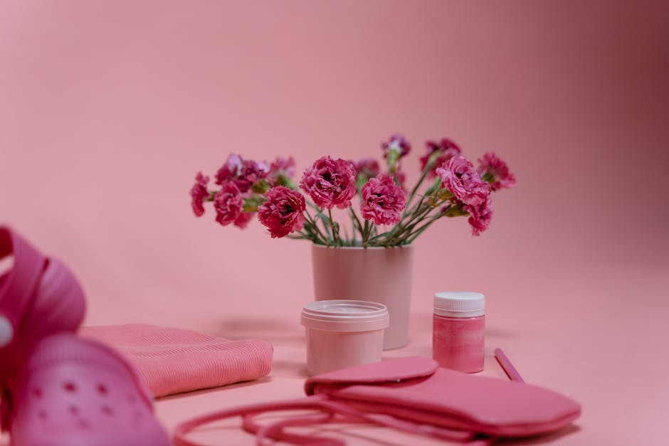 Beautiful pink flowers in pot surrounded by pink accessories on a pastel backdrop.