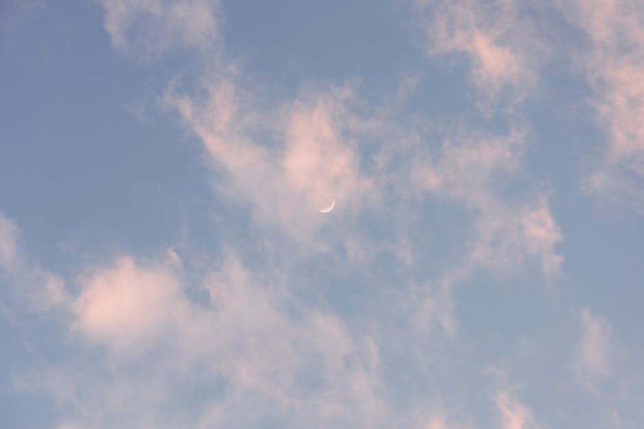 A tranquil scene of a crescent moon in a blue, cloudy sky.