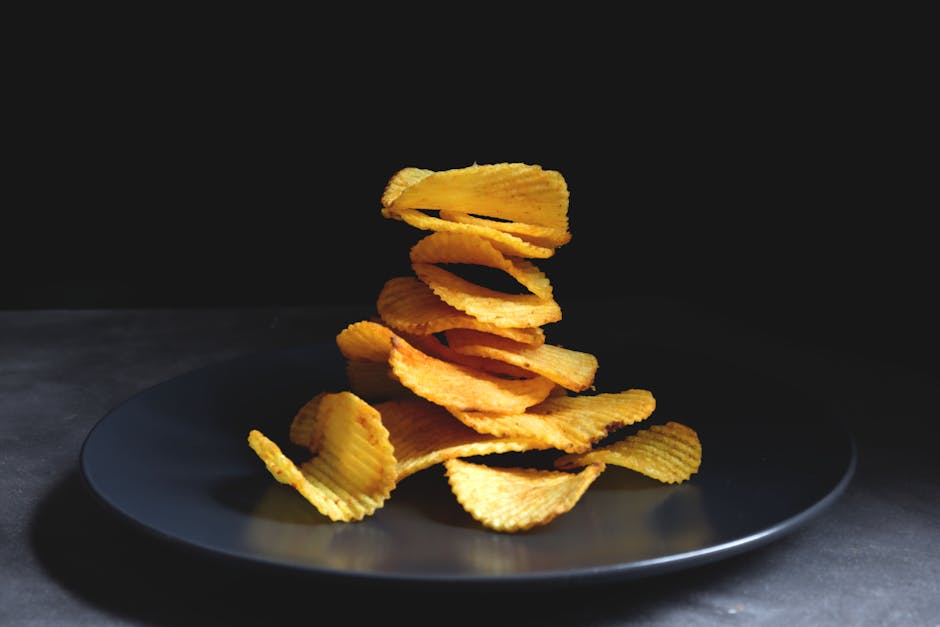 A delicious stack of golden ripple potato chips placed on a sleek black plate.