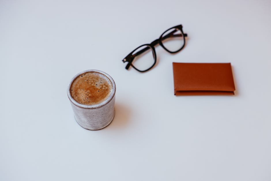 Minimalist flat lay of coffee, eyeglasses, and wallet on a white background.