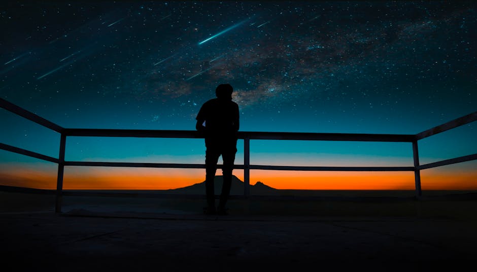 A silhouette of a person observing a vibrant night sky with stars and meteors.