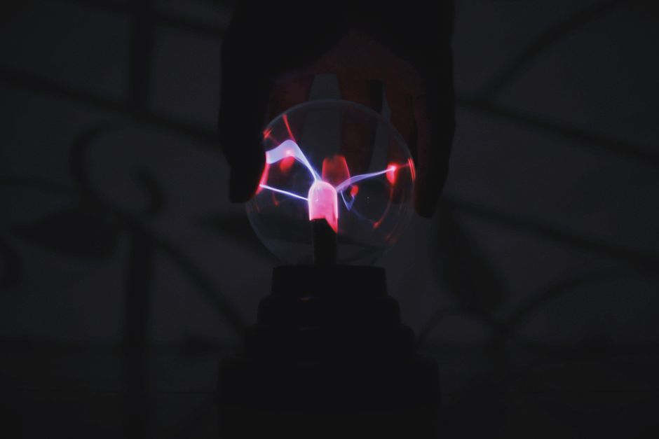 Crop anonymous person touching plasma ball with magic colorful light in dark room
