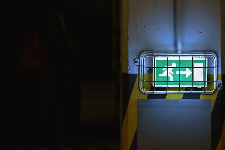 Green emergency exit sign with arrow in dimly lit area, emphasizing safety.