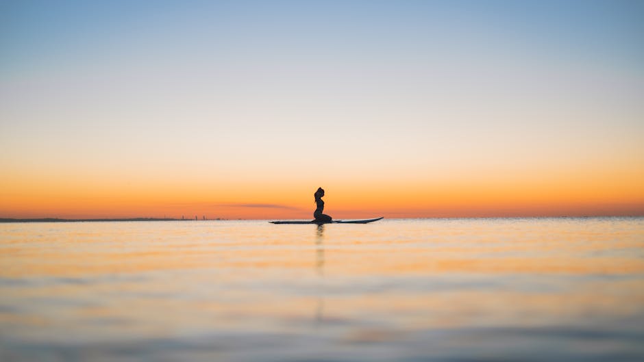 A serene silhouette of a woman meditating on a surfboard during a stunning sunset, conveying tranquility.