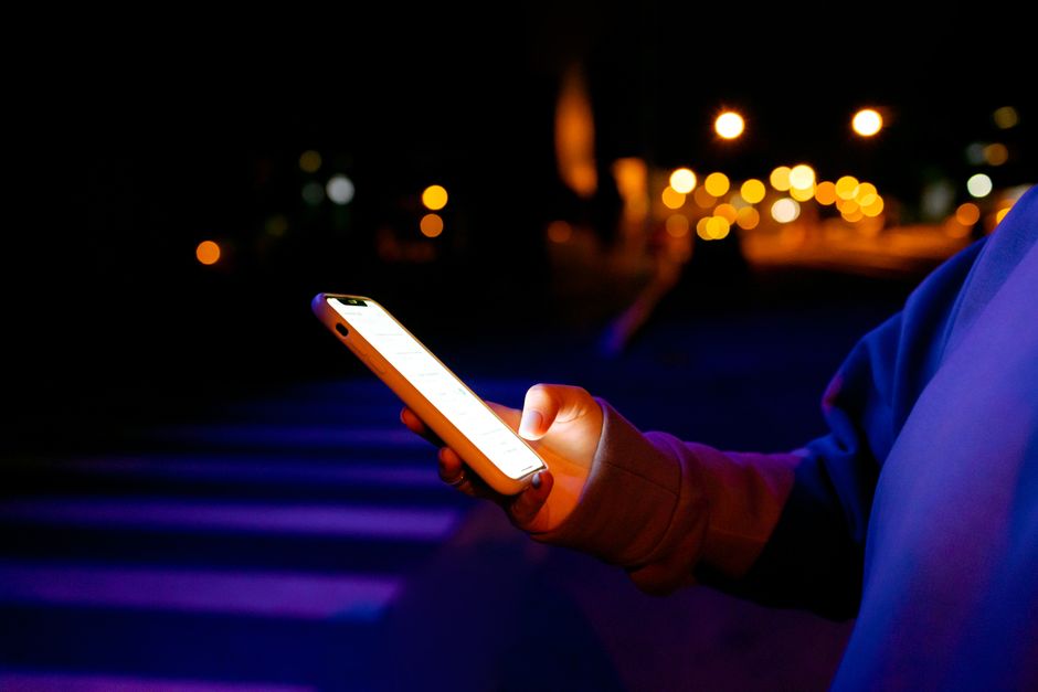 A person holds a glowing smartphone outdoors at night with bokeh lights in the background.