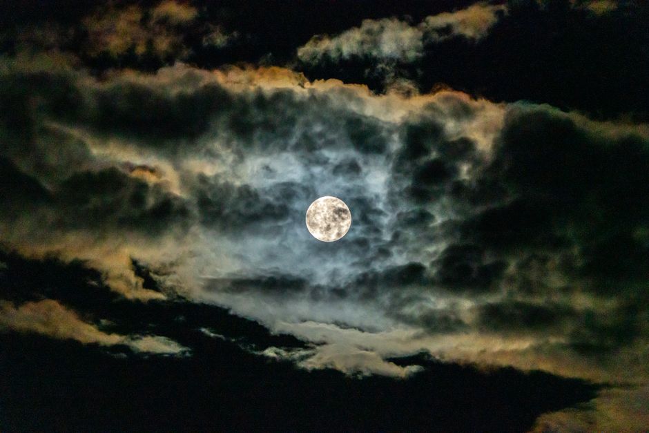 Captivating full moon shining through dramatic clouds at night, creating a mystical and atmospheric sky scene.
