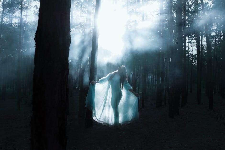 A woman in a flowing dress stands in a mystical forest with sunlight rays breaking through.