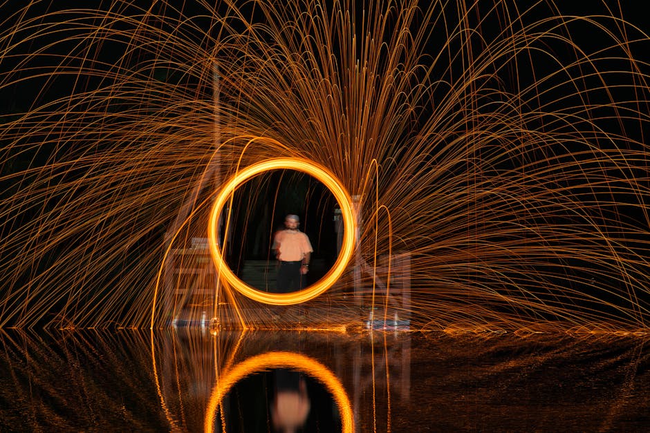 Dynamic light painting with steel wool creating vibrant reflections over water at night.