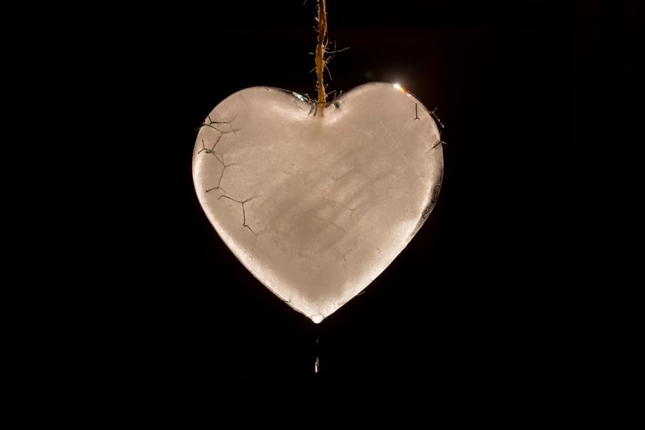 A cracked heart-shaped ice sculpture hanging by a string in darkness.