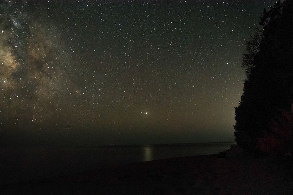 Peaceful starry night sky overlooking a tranquil sea and coastal landscape.