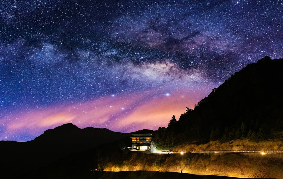 Stunning view of the Milky Way over a serene mountain landscape with a lit house at night.
