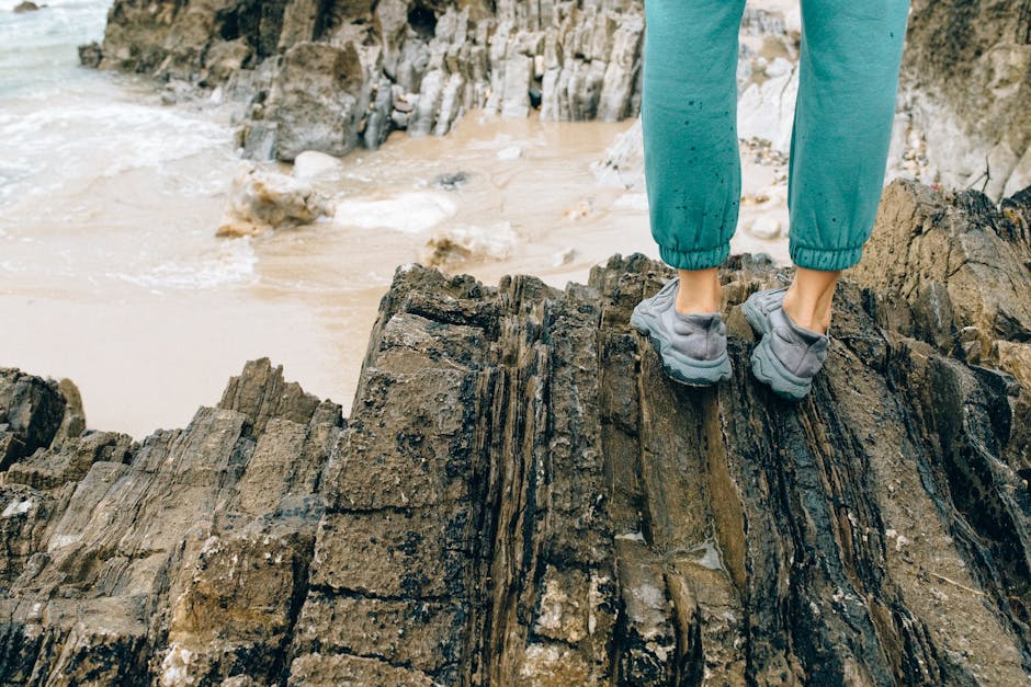 A person in sneakers standing on rugged rocks by a sandy seashore, exploring the coastal scenery.
