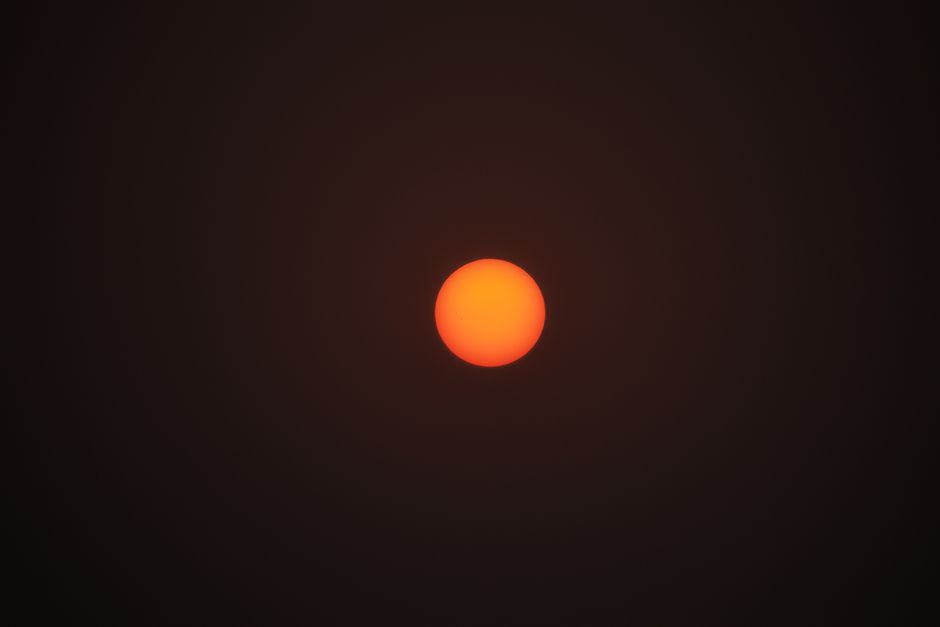 A vivid, bright orange sun set against a contrasting black background, ideal for space-themed designs.
