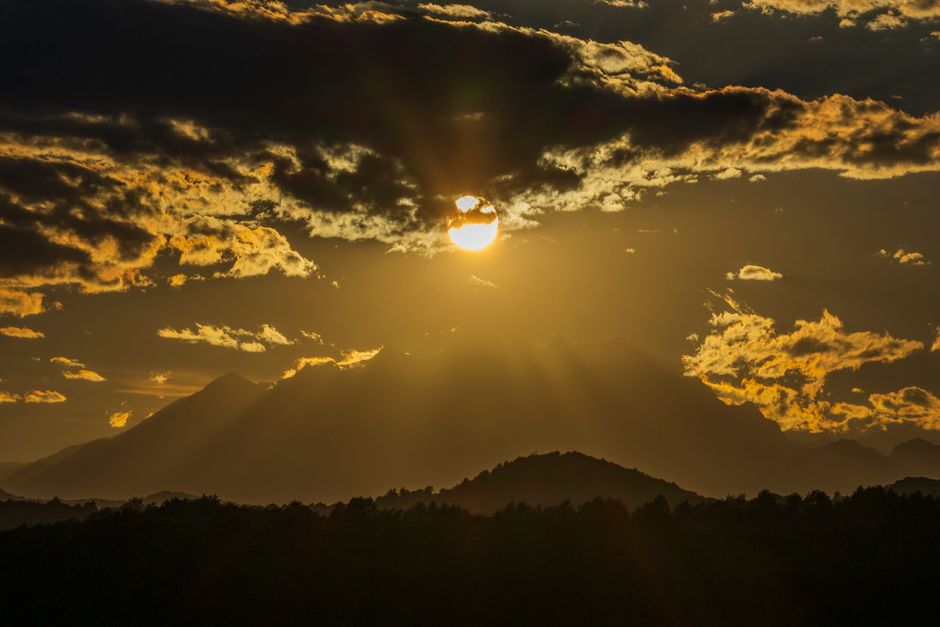 Golden sunset casting dramatic shadows over mountain peaks with stunning cloud formations.