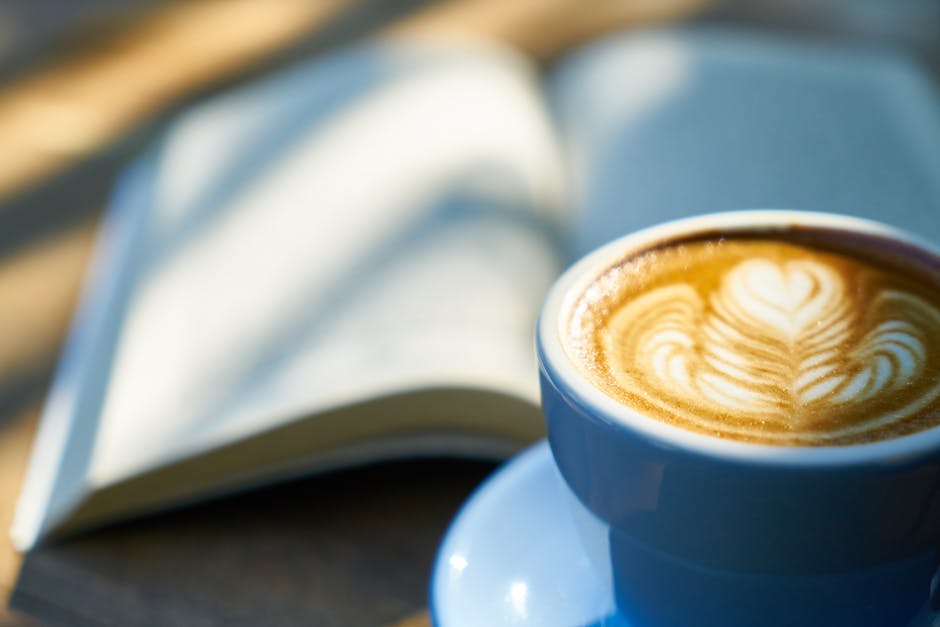 Warm latte art in a blue cup beside an open book, capturing a cozy morning vibe.