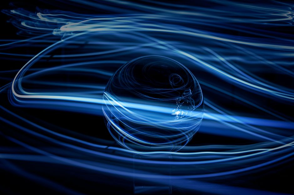 Abstract close-up of swirling blue light trails around a glass sphere, creating a dynamic visual effect.